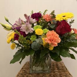 Mixed bouquet in a clear glass vase with roses, lilies, carnations, and daisies