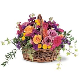 Bright mixed arrangement of roses and blooms in pink, purple, orange, and yellow in a wicker basket