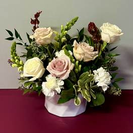 Arrangement of pale roses and white carnations in a white container