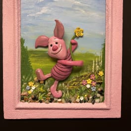 Pink pig figurine holding a yellow flower in a painted frame