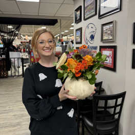 Woman holding a pumpkin vase filled with orange and purple flowers