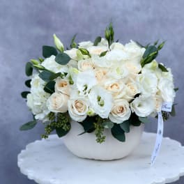 White roses and lisianthus arranged in a white bowl vase
