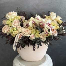 Cream roses and spotted orchids in a round blush vase