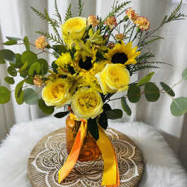 Yellow roses and sunflowers in an amber vase with orange ribbon