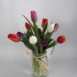 Mixed tulips in red, pink, purple, and white arranged in a clear glass jar tied with raffia.