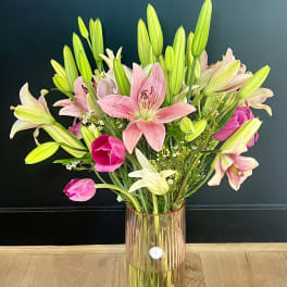 Pink and white lilies with tulips in a tall glass vase
