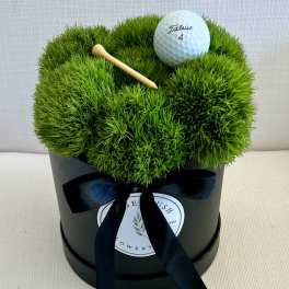 Green moss arrangement in a black box with a golf ball and tee
