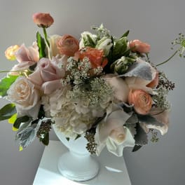 Blush and white floral arrangement in a white pedestal vase