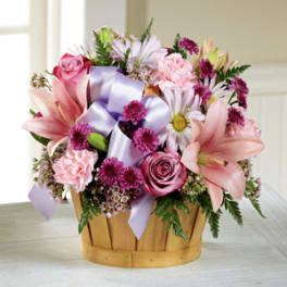 Pink and lavender flower arrangement in a wooden basket with ribbon