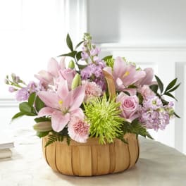Pink lilies and mixed blooms arranged in a wooden basket
