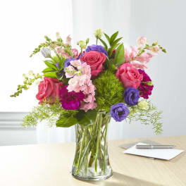Mixed pink, purple, and white flowers in a clear glass vase