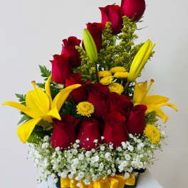 Red roses and yellow lilies arranged in a black container with white filler flowers.