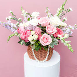 Pink and white rose arrangement in a wicker basket with pearl trim