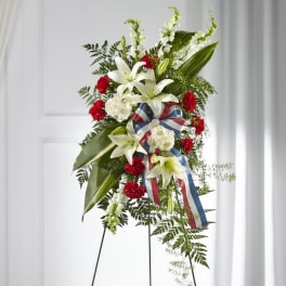 Standing floral spray with white lilies, red carnations, and a patriotic ribbon