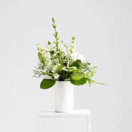 White and green floral arrangement in a tall white ribbed vase on a white pedestal