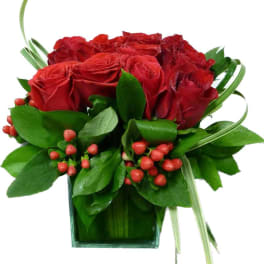 Red roses in a square glass vase with green foliage and red berries