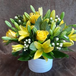Yellow lilies and roses arranged in a white vase