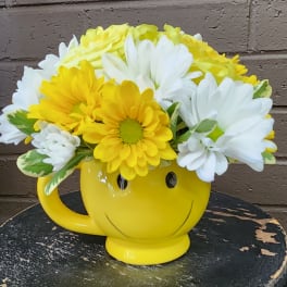 Yellow smiley-face mug filled with white and yellow daisies
