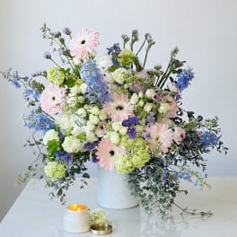 Pastel floral arrangement in a white vase with a lit candle nearby