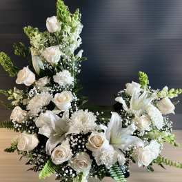 Tall crescent-shaped arrangement of white roses, lilies, and mums with green accents
