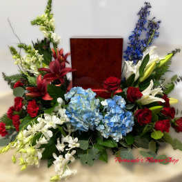 Red, white, and blue sympathy arrangement surrounding a wooden urn on a draped table