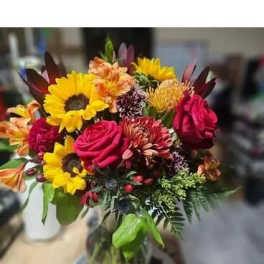 Bright mixed bouquet with sunflowers, roses, and chrysanthemums in a glass vase