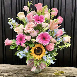 Tall mixed bouquet of pink roses and gerbera daisies with a sunflower in a glass vase
