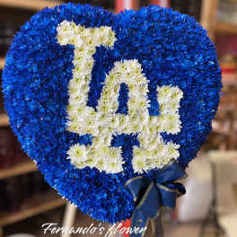 Heart-shaped blue and white floral standing spray with a monogram design and blue ribbon bow.