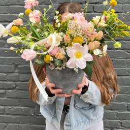 Large pastel flower arrangement in a gray vase held by a person