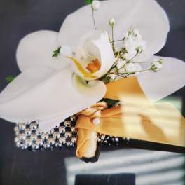 White orchid wrist corsage with small white blooms, gold ribbon, and rhinestone bracelet.