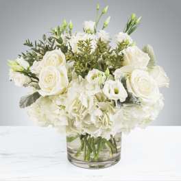 Low arrangement of white roses, lisianthus, and hydrangeas in a clear glass vase.