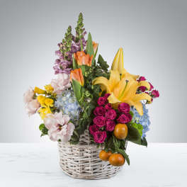 Colorful mixed flower basket with yellow lilies, pink spray roses, tulips, hydrangeas, and oranges.