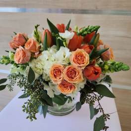 Low arrangement of peach roses and tulips with white hydrangeas in a glass vase