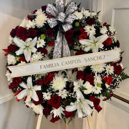 Standing round wreath of red roses, white lilies, and white mums with script ribbon on an easel