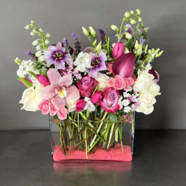 Mixed pink, white, and purple flowers arranged in a clear rectangular vase
