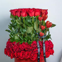 Red roses arranged in a glittery red box with heart picks