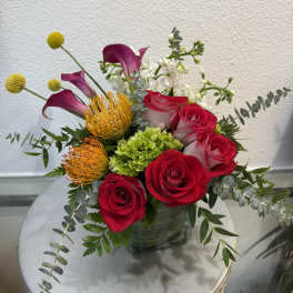 Mixed bouquet with red roses, purple calla lilies, and orange pincushion blooms in a vase