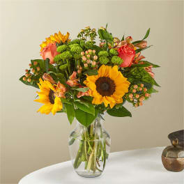 Bouquet of sunflowers, pink roses, and green button mums in a glass vase
