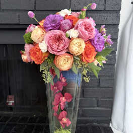 Tall floral arrangement in a clear glass vase with pink, orange, and purple blooms