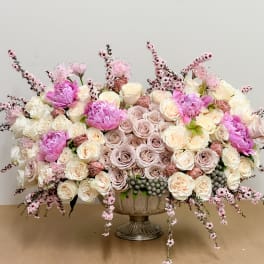 Large pastel floral arrangement in a pedestal vase with pink and cream roses