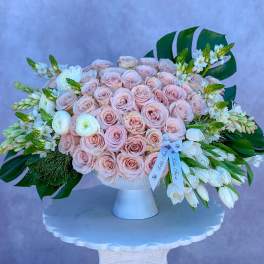 Low compote of blush roses with white tulips and large tropical leaves in a white pedestal vase
