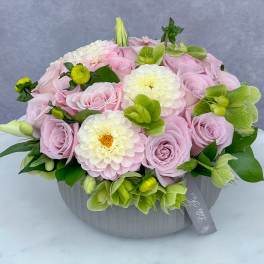 Pink roses and white blooms arranged in a gray round box