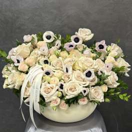 Cream rose arrangement in a low white vase with pale anemones