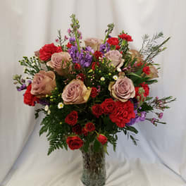 Mixed bouquet of roses, carnations, and purple flowers in a glass vase