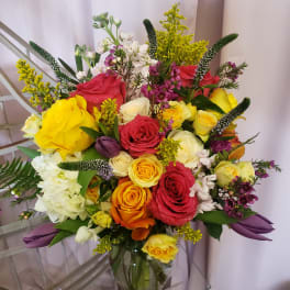 Mixed bouquet of roses, white blooms, and purple accents in a glass vase