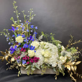 Large floral arrangement with white roses, hydrangeas, and blue flowers in a wooden box