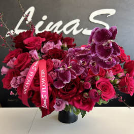 Bouquet of red roses and purple orchids in a black vase