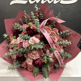 Bouquet of pink roses and dark red flowers wrapped in pink paper