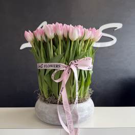 Pink tulips arranged in a round gray planter with a pink ribbon