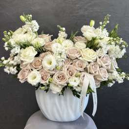 Cream and blush rose arrangement in a white vase with a ribbon